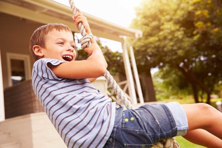 Young boy swinging in the outdoors who and is participating in a pediatric clinical research study.